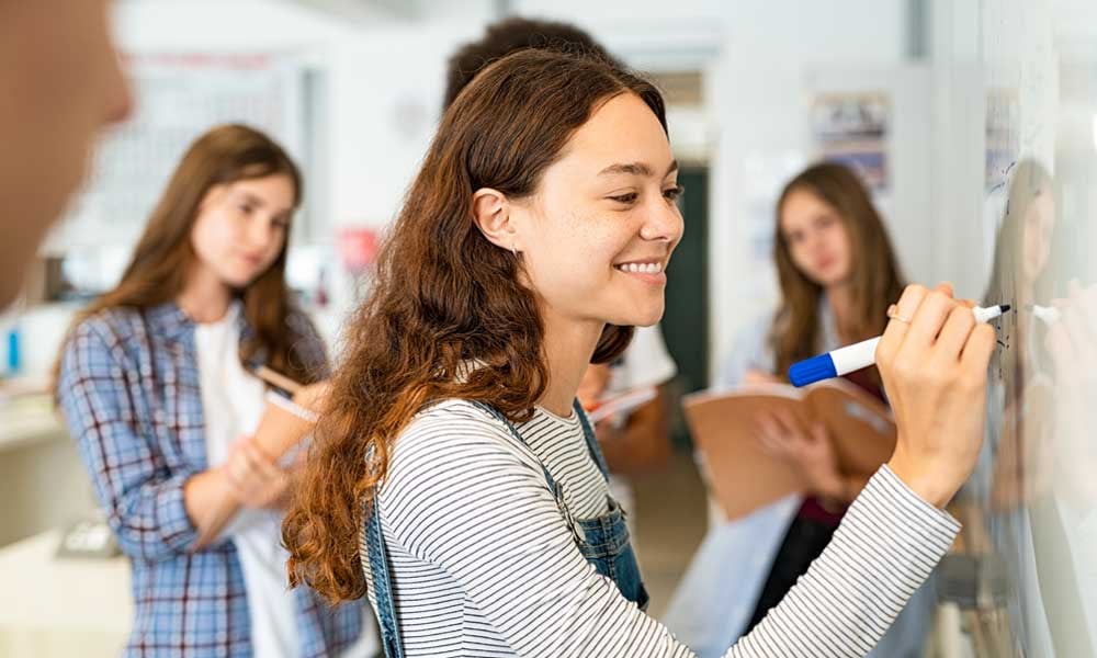 FUNDAÇÃO ROGE: uma aluna escrevendo no quadro e outro grupo fazendo anotações da interdisciplinaridade na educação